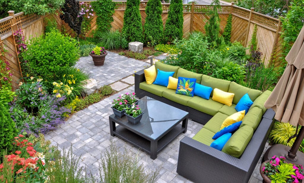 A beautiful small, urban backyard garden featuring a tumbled paver patio, flagstone stepping stones, and a variety of trees, shrubs and perennials add colour and year round interest.